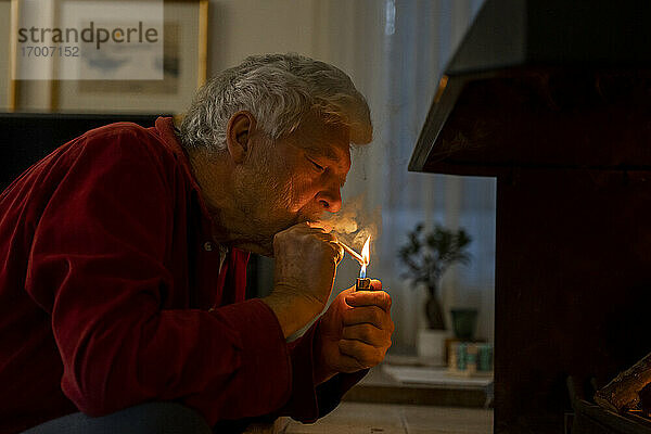 Älterer Mann zündet Zigarette mit Feuerzeug an  während er zu Hause sitzt