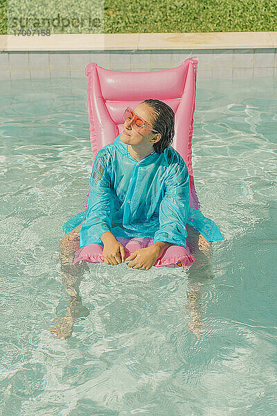Frau in blauem Regenmantel entspannt sich auf rosa Luftmatratze im Schwimmbad