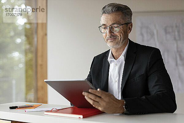 Älterer Geschäftsmann  der zu Hause sitzend ein digitales Tablet benutzt