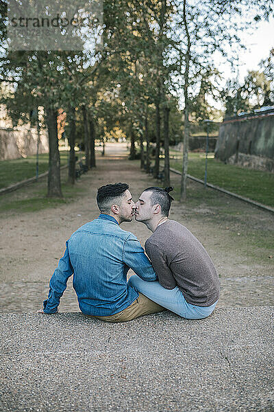 Zärtliches schwules Paar küsst sich auf dem Fußweg in einem öffentlichen Park