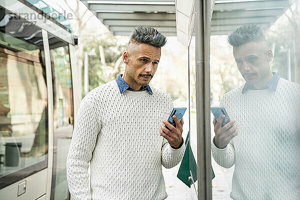 Spiegelung eines männlichen Unternehmers  der ein Smartphone am Bahnhof hält