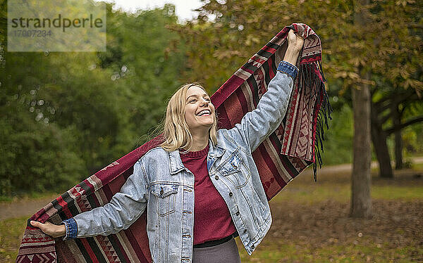 Glückliche Frau mit Schal im herbstlichen Park stehend
