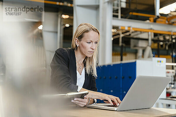 Unternehmerin arbeitet am Laptop  während sie in einer Fabrik sitzt