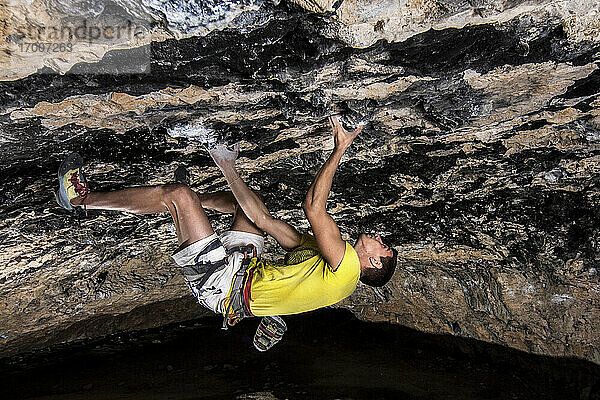 Junger männlicher Sportler klettert mühsam in einer Höhle auf einen Felsen