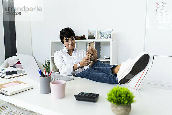 Porträt einer Geschäftsfrau  die mit ihrem Smartphone am Bürotisch Pause macht