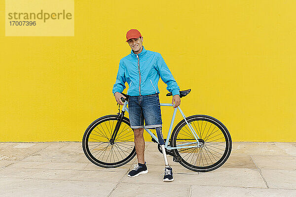 Männer mit Mütze  die ein Fahrrad halten und an einer gelben Wand stehen