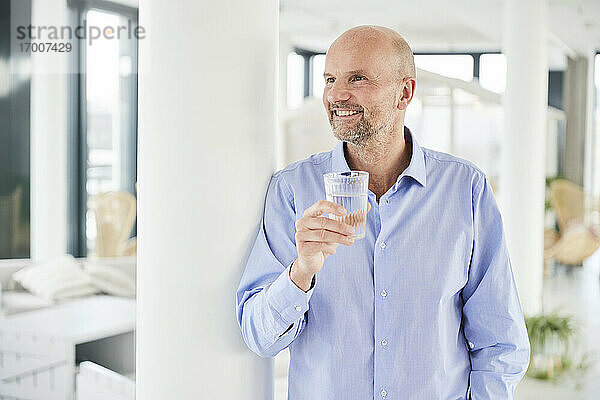 Lächelnder Geschäftsmann  der Wasser trinkt  während er zu Hause steht
