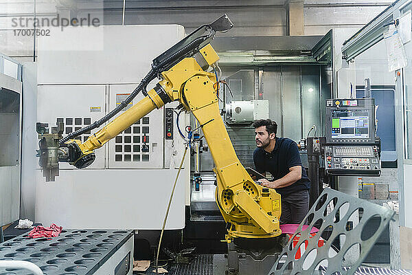 Junger männlicher Arbeiter  der einen Roboterarm in einer Produktionsstätte analysiert