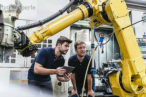 Männliche Mitarbeiter diskutieren über einen Roboterarm in einer Fabrik