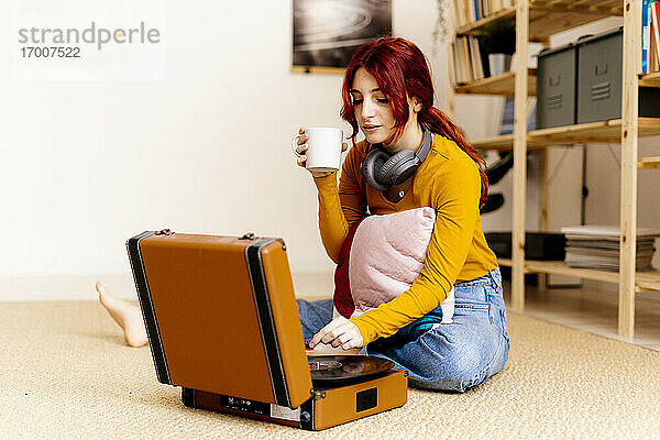 Junge Frau trinkt Kaffee und benutzt einen Plattenspieler zu Hause