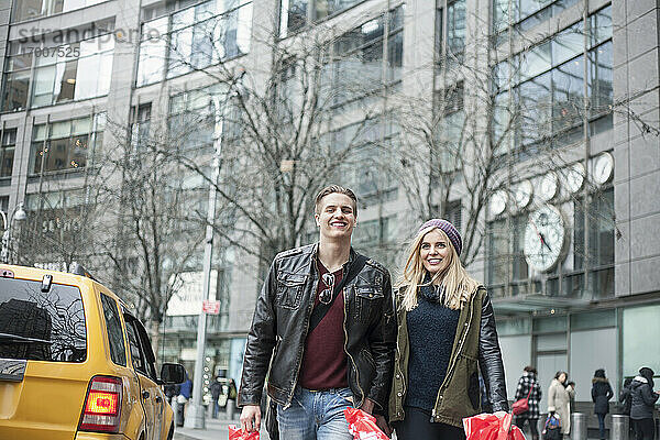 Lächelndes Paar mit Einkaufstaschen beim Spaziergang auf der Straße in der Stadt