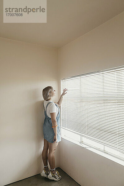 Junge Frau blickt durch die Jalousien auf das Fenster