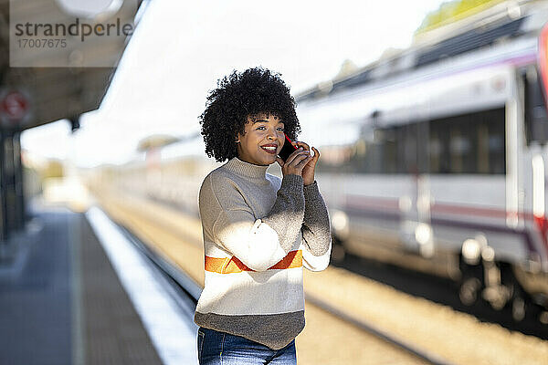 Glückliche Frau  die mit ihrem Handy telefoniert  während sie am Bahnhof wartet
