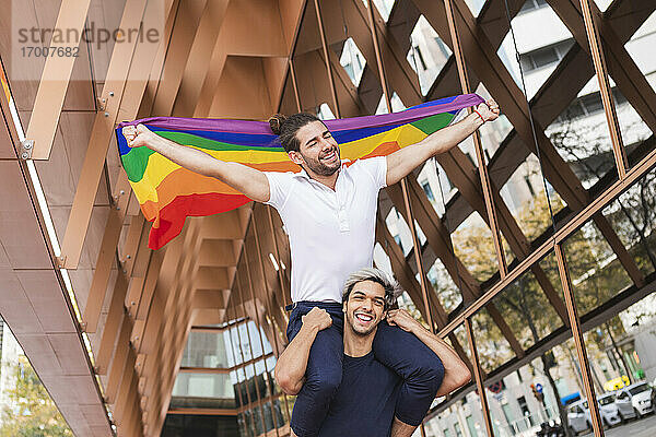 Lächelnder Mann trägt Partnerin mit Regenbogenschal auf den Schultern in der Stadt