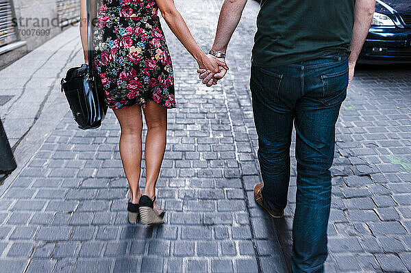 Freundin und Freund halten Hände auf der Straße in der Stadt gehen