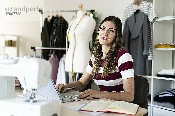 Lächelnde Geschäftsfrau mit Laptop auf dem Schreibtisch sitzend im Studio