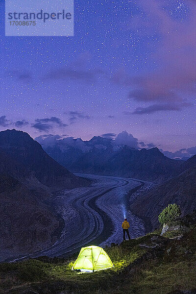 Wanderer Mann mit Stirnlampe Beleuchtung der Sternenhimmel in der Nähe von Zelt durch den Aletschgletscher  Berner Alpen  Wallis Kanton  Schweiz  Europa