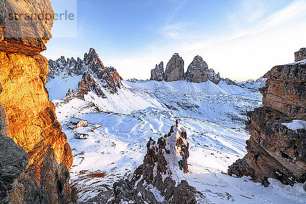 Mann auf Felsen bewundert den verschneiten Monte Paterno und die Drei Zinnen bei Sonnenuntergang  Sextner Dolomiten  Südtirol  Italien  Europa