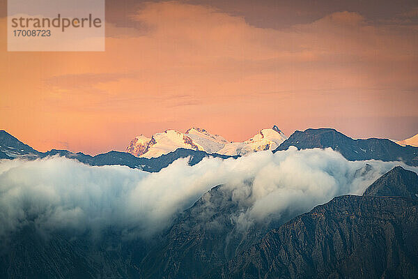 Brennender Himmel bei Sonnenaufgang über dem schneebedeckten Monte Rosa  umgeben von einem Meer aus Wolken  Kanton Wallis  Schweiz  Europa