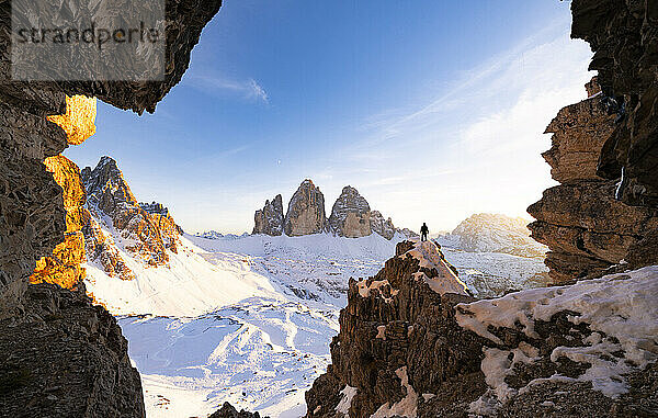 Wanderer auf Felsen mit Blick auf die Drei Zinnen und den schneebedeckten Monte Paterno bei Sonnenuntergang  Sextner Dolomiten  Südtirol  Italien  Europa