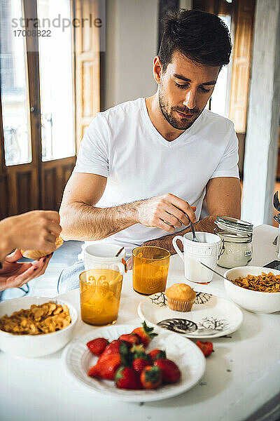 Junger Mann sitzt am Tisch und frühstückt zu Hause