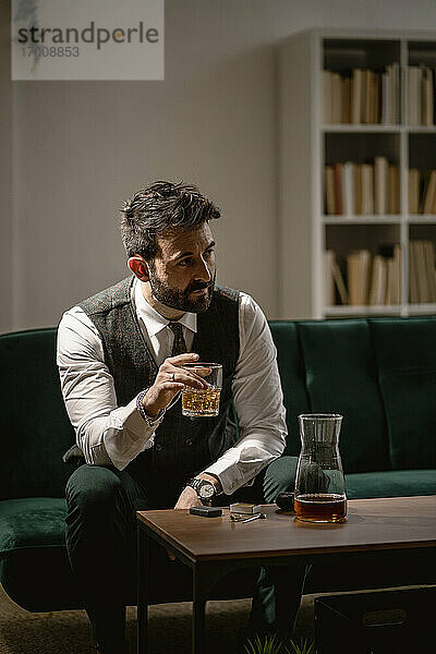 Porträt eines gut gekleideten Mannes  der im Wohnzimmer Whiskey trinkt