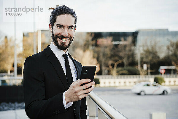 Geschäftsmann lächelnd bei der Verwendung eines Mobiltelefons in der Stadt stehend
