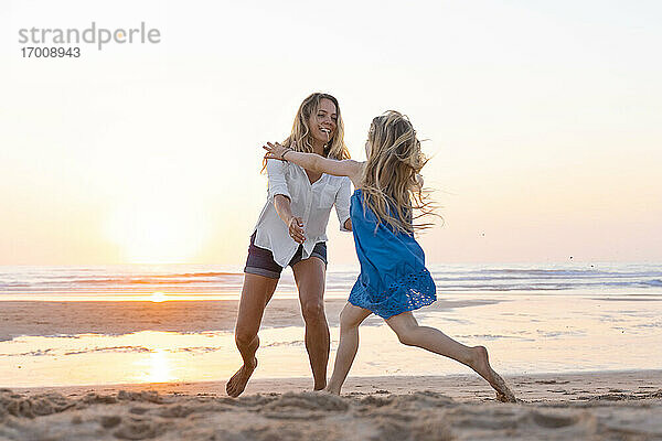 Mutter und Tochter genießen beim Spielen am Strand bei Sonnenuntergang
