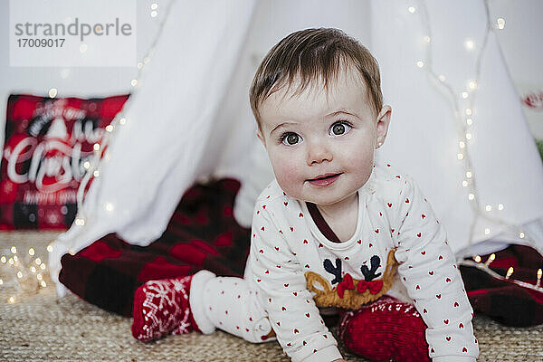 Niedliches kleines Mädchen  das lächelnd an einem Zelt sitzt  während Weihnachten zu Hause