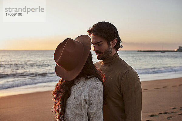 Paar steht bei Sonnenaufgang von Angesicht zu Angesicht am Strand