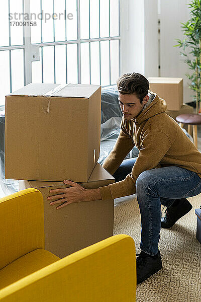 Junger Mann ordnet Kartons im Wohnzimmer einer neuen Wohnung