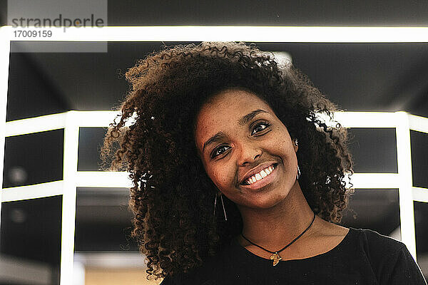 Lächelnde junge Afro-Frau an der Wand in der Stadt
