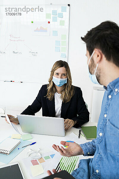 Geschäftsleute mit Schutzmasken bei der Arbeit im Büro
