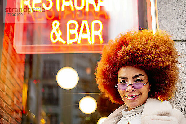 Lächelnde schöne Frau mit Afro-Haar und Sonnenbrille vor einem Restaurant