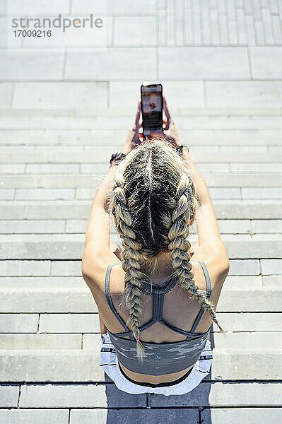 Sportlerin  die auf einer Treppe sitzend ein Mobiltelefon benutzt