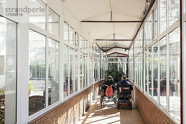 Behinderter Mann und Frau im Rollstuhl auf dem Flur eines Pflegeheims