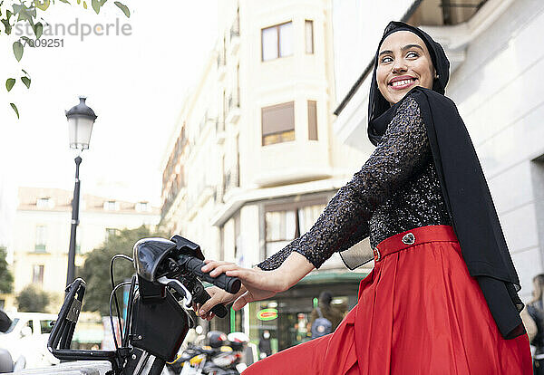 Porträt einer jungen Frau mit Hidschab  die auf einem Mietfahrrad sitzt