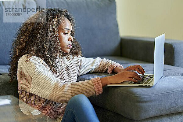 Junge Frau mit lockigem Haar benutzt Laptop im Wohnzimmer zu Hause