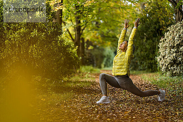 Sportler mit erhobener Hand beim Yoga  während er auf einem Fußweg im Park trainiert