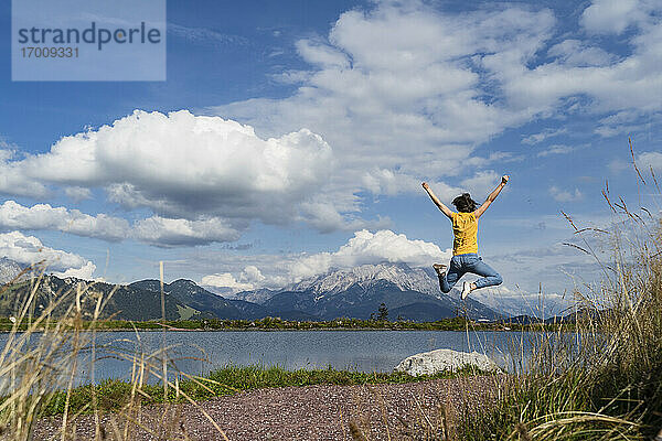 Junge Frau springt am Ufer eines Bergsees im Frühling