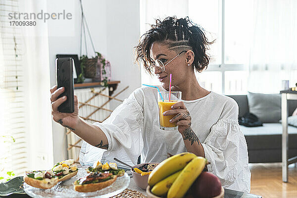 Porträt einer jungen Frau  die ein Selfie mit ihrem Smartphone macht  während sie frühstückt