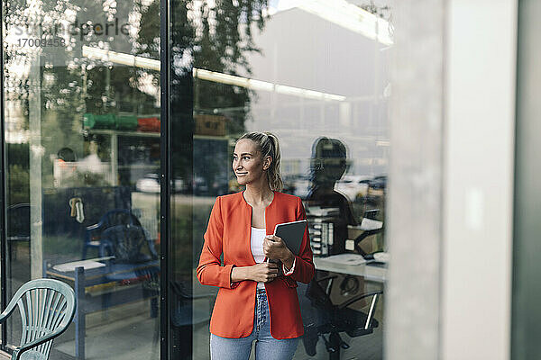 Lächelnde Geschäftsfrau mit digitalem Tablet an einer Glaswand