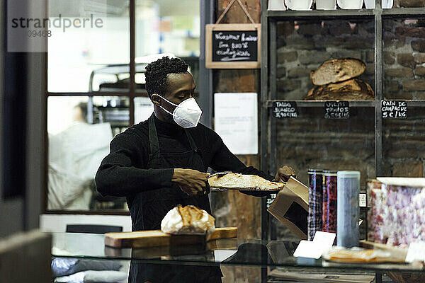 Männlicher Bäckereibesitzer verpackt Brot in eine Papiertüte  während er in der Bäckerei steht