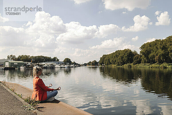 Geschäftsfrau meditiert am Seeufer gegen den Himmel
