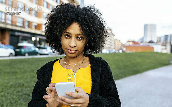 Junge Frau mit Afro-Haar  die ein Mobiltelefon benutzt  während sie in der Stadt steht