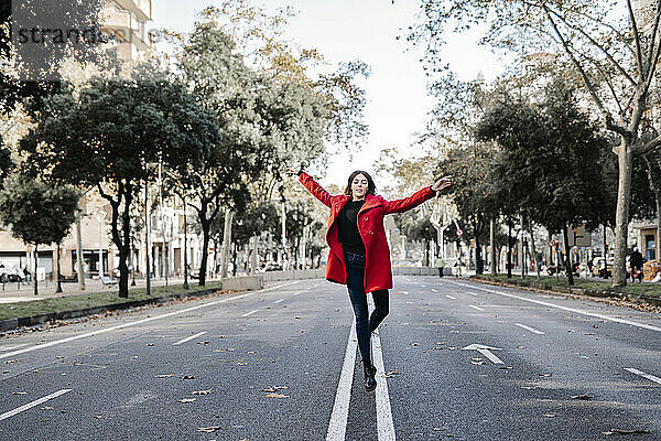 Unbekümmerte Frau in roter Jacke tanzt und springt auf der Straße