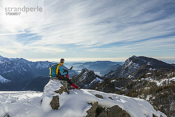 Männlicher Wanderer  der sein Handy benutzt  während er auf einem Berg gegen den Himmel sitzt  Orobic-Alpen  Lecco  Italien