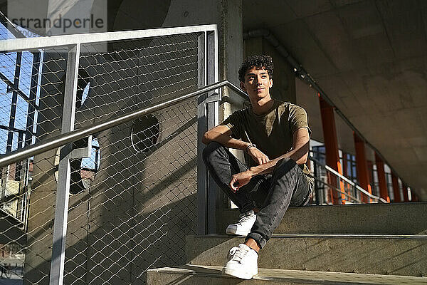 Nachdenklicher junger Mann  der an einem sonnigen Tag auf einer Treppe sitzt