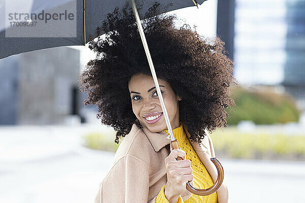 Junge Frau lächelt  während sie einen Regenschirm hält und im Freien steht