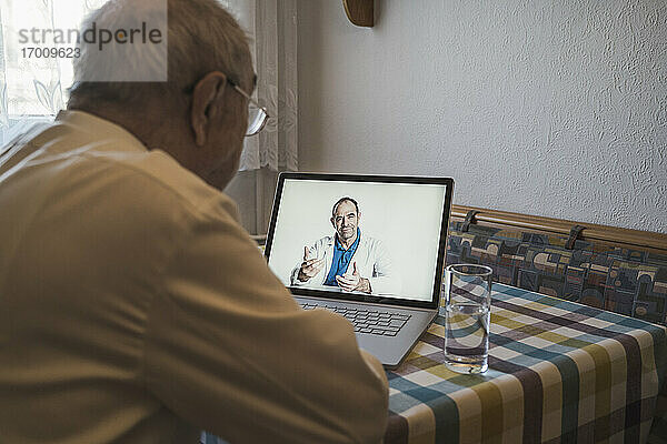 Ein älterer Mann lässt sich von einem männlichen Allgemeinmediziner über einen Laptop per Videoanruf zu Hause beraten